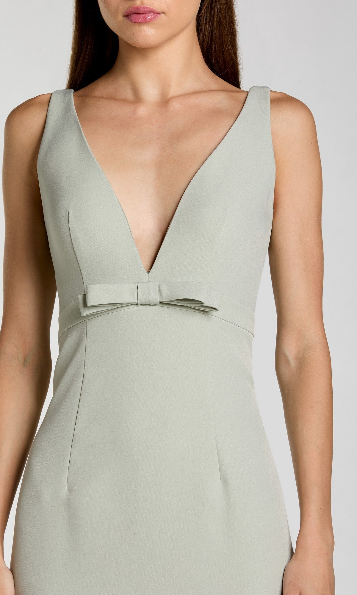 A woman wears the Long Formal Dress: Mac Duggal 2371, a sleeveless light gray crepe dress with a deep V-neckline and a bow at the waist.